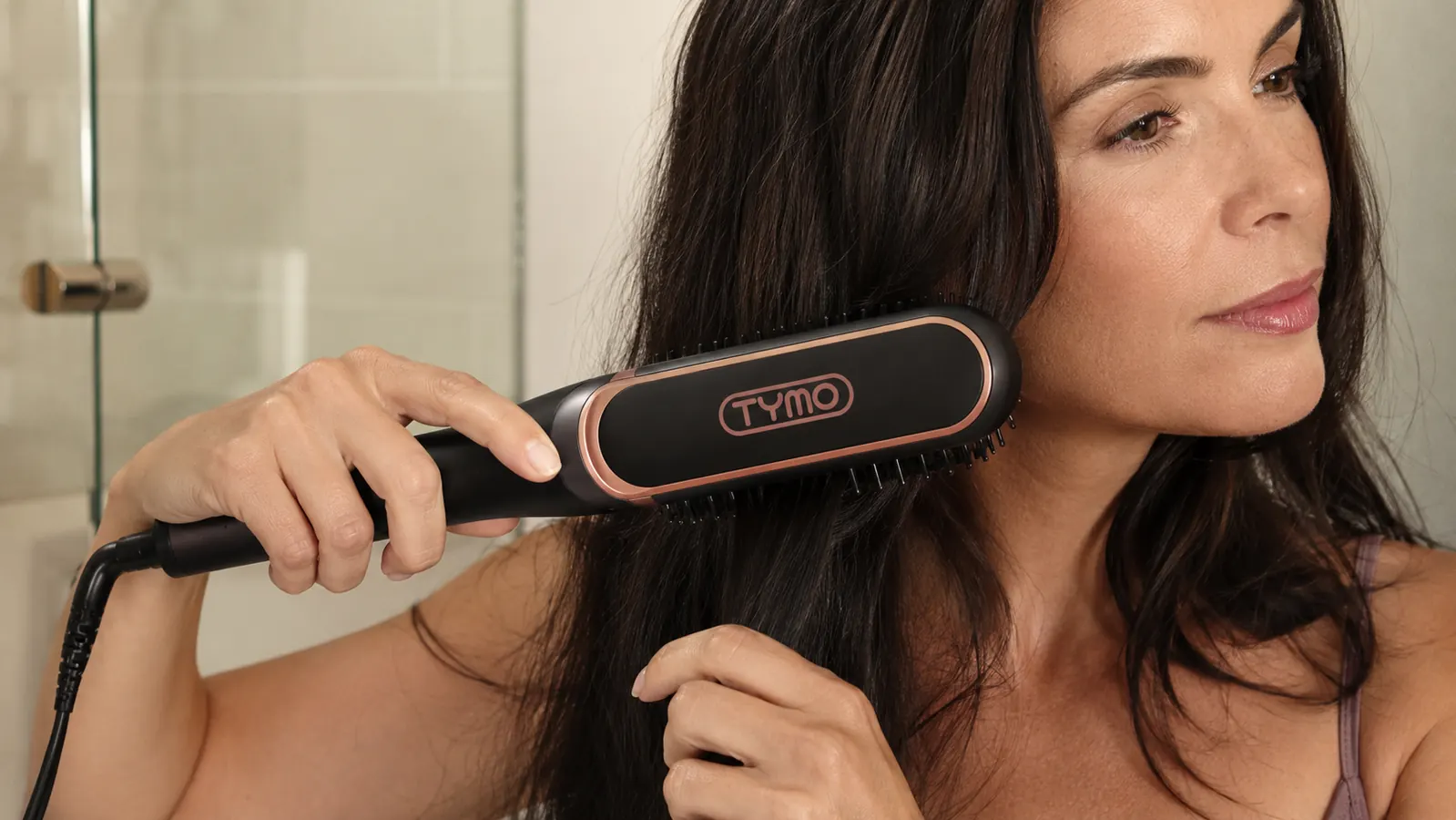Close-up of a hand holding the TYMO Ring straightener brush against a section of hair, showing the bristles and heating plate