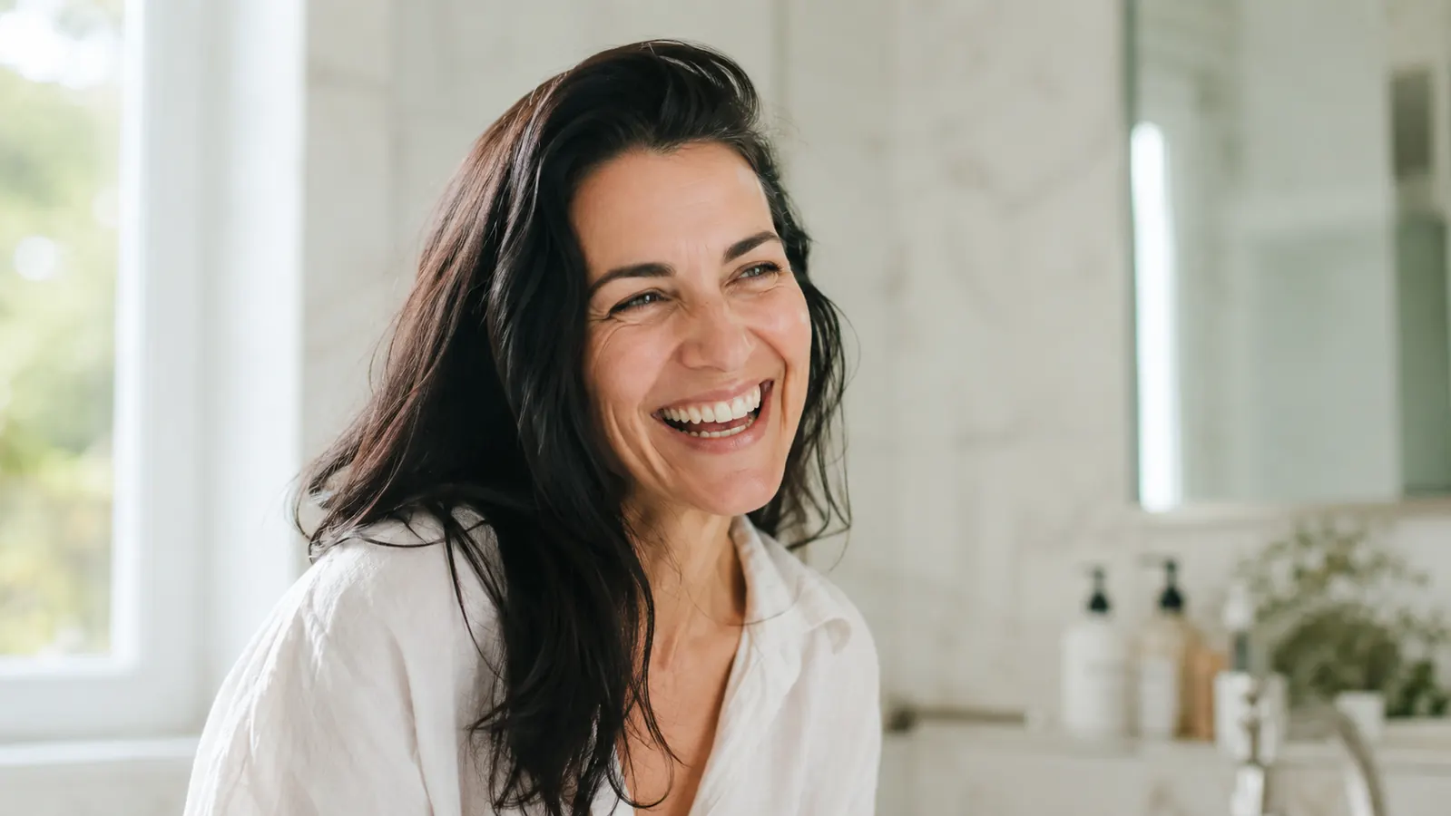 Woman with dark hair laughing outdoors on day three of her hair, no visible greasy roots