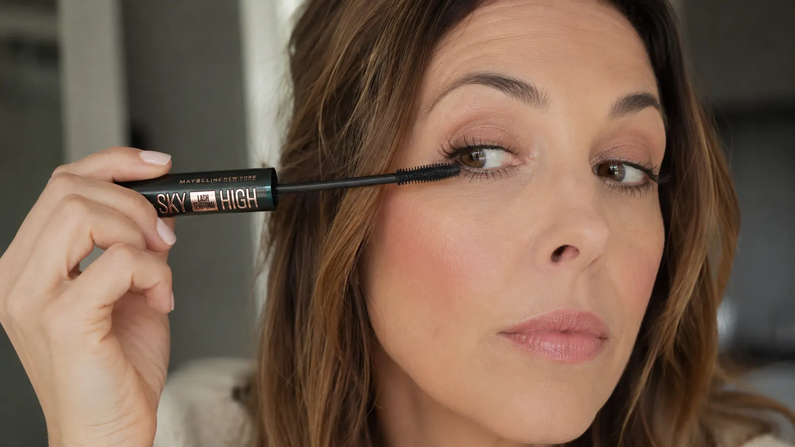 Close-up of a hand wiggling a mascara wand at the base of the lashes before sweeping upward