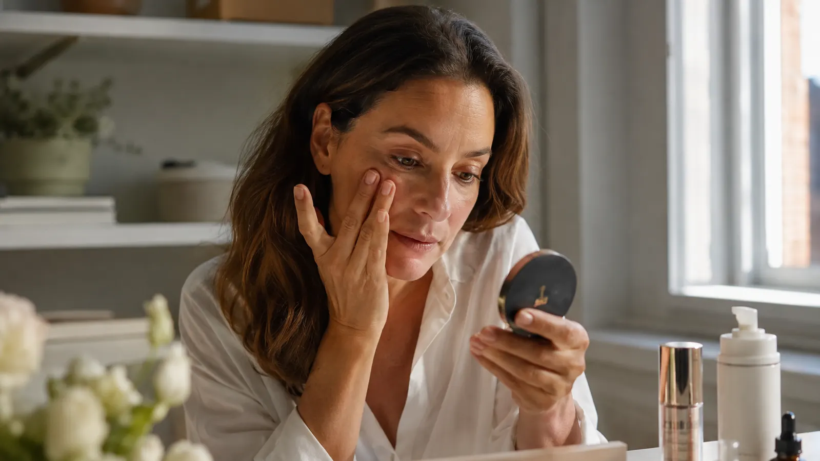 Woman checking her mascara in a small compact mirror at her office desk in the late afternoon