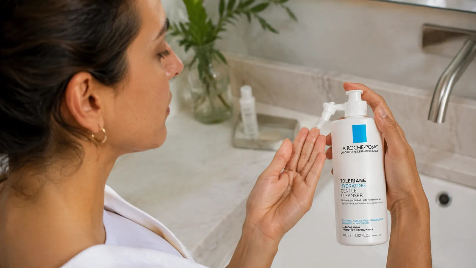Hand dispensing La Roche-Posay Toleriane cleanser onto fingertips over a sink