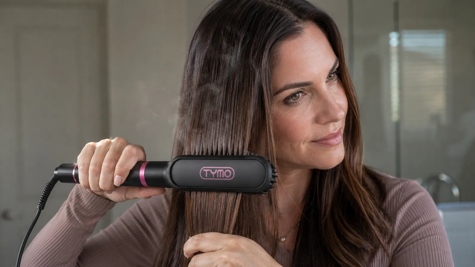 Close-up of the TYMO Ring straightener brush bristles pressed against a thick section of dark hair mid-stroke